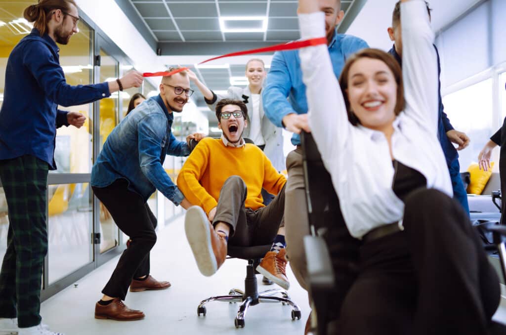 Friendly work team ride chairs in office room cheerfully.