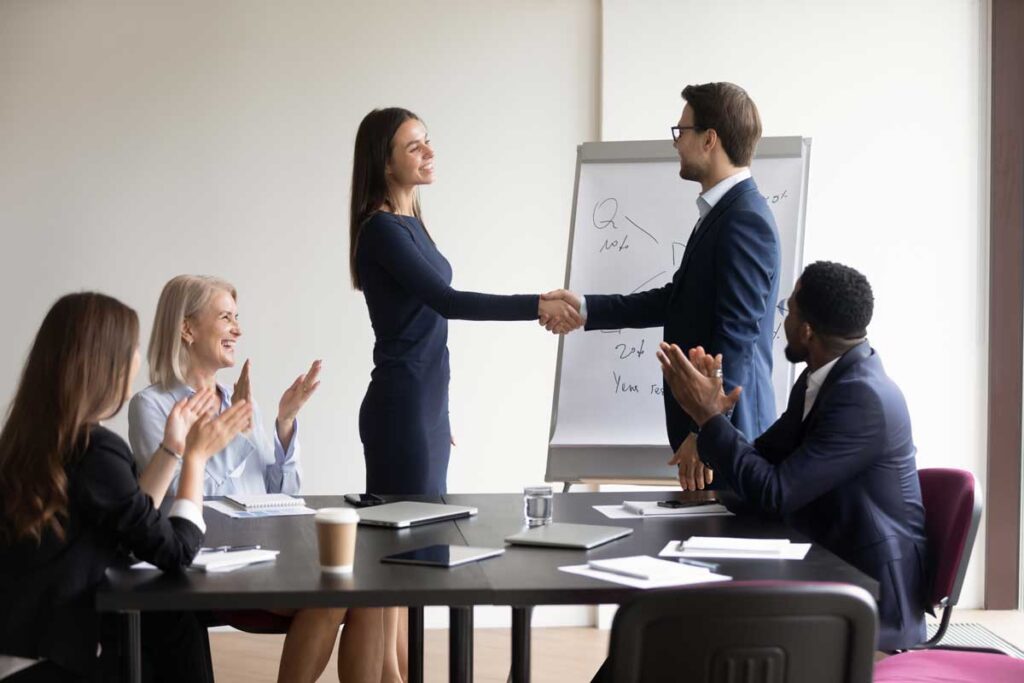Happy excited promoted employee shaking hands with boss. Business leader hiring new team member, welcoming worker, thanking manager for good work. Diverse team applauding coworker success